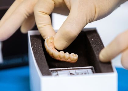 Eine Zahnprothese wird von einer Hand im weißen Handschuh in ein Kästchen gelegt.