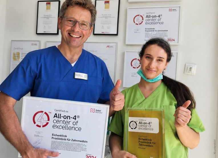 Zwei Zahnmediziner halten stolz ihre Zertifikate der "All-on-4"-Exzellenz in der Eichenklinik.