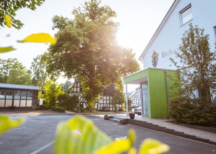 Auf der linken Seite des Bildes ist der grüne Eingangsbereich der Eichenklinik zu sehen. Im Fokus ist ein großer Eichenbaum so wie die Umgebung um die Praxis.