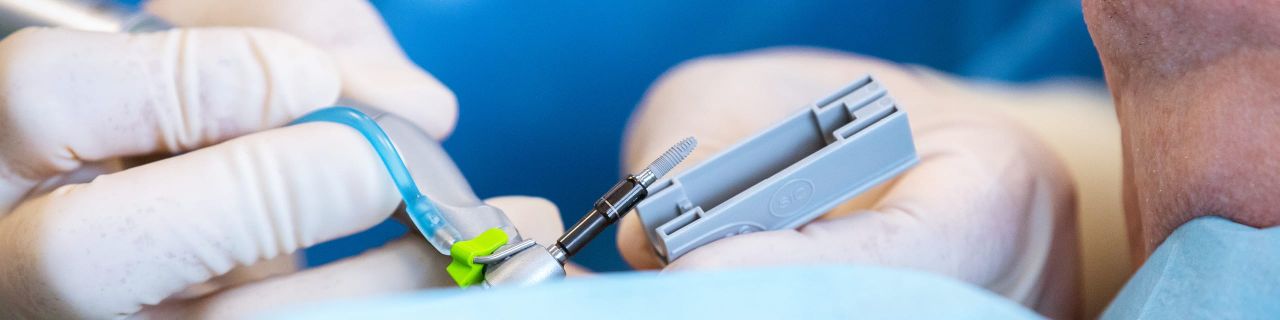 Hände in weißen Handschuhen halten einen Dentalbohrer während einer präzisen zahnärztlichen Behandlung.