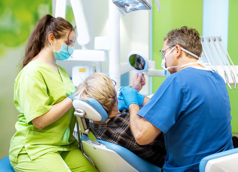 Zahnmediziner und ZMFAs führen eine Prophylaxe-Behandlung bei einem Patienten in der Zahnarztpraxis durch. | © Name