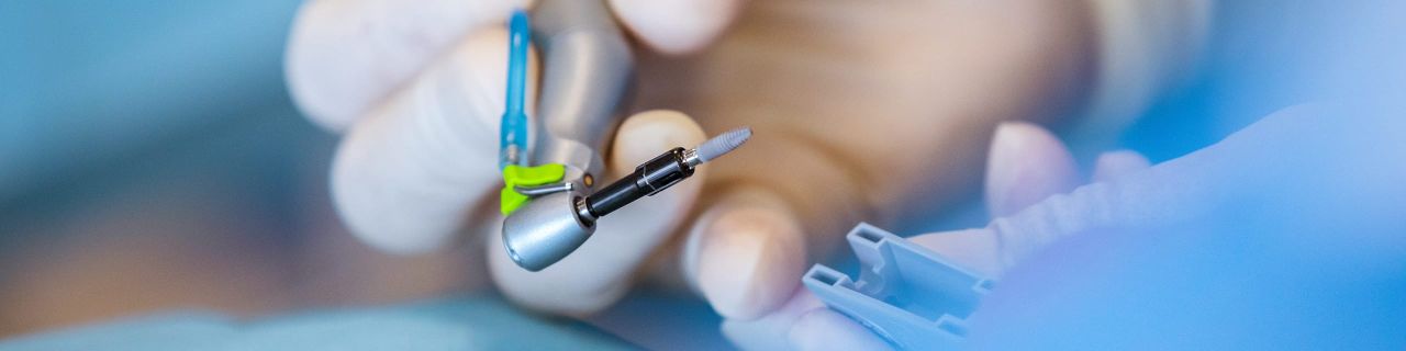 Eine Hand im weißen Handschuh führt ein zahnärztliches Instrument.